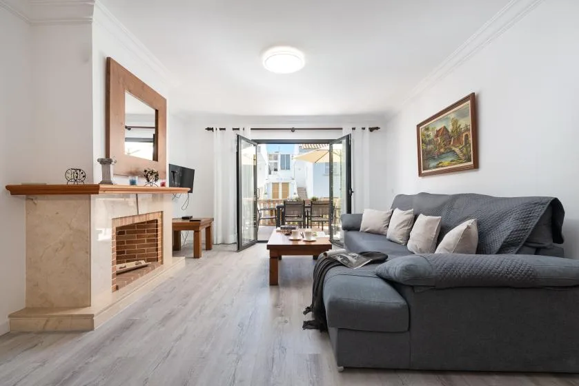 A bright living room with seating, a coffee table, and glass doors opening to a balcony.