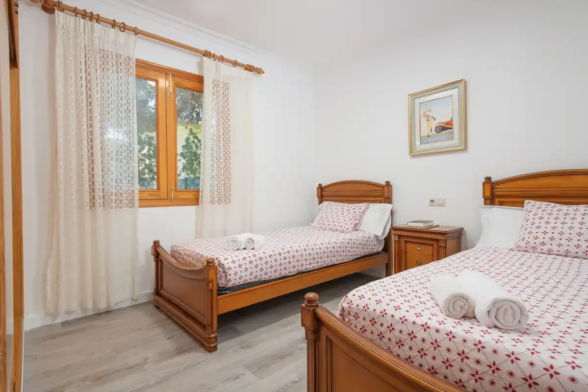 A bedroom with two wooden beds, patterned bedding, and a window with curtains.