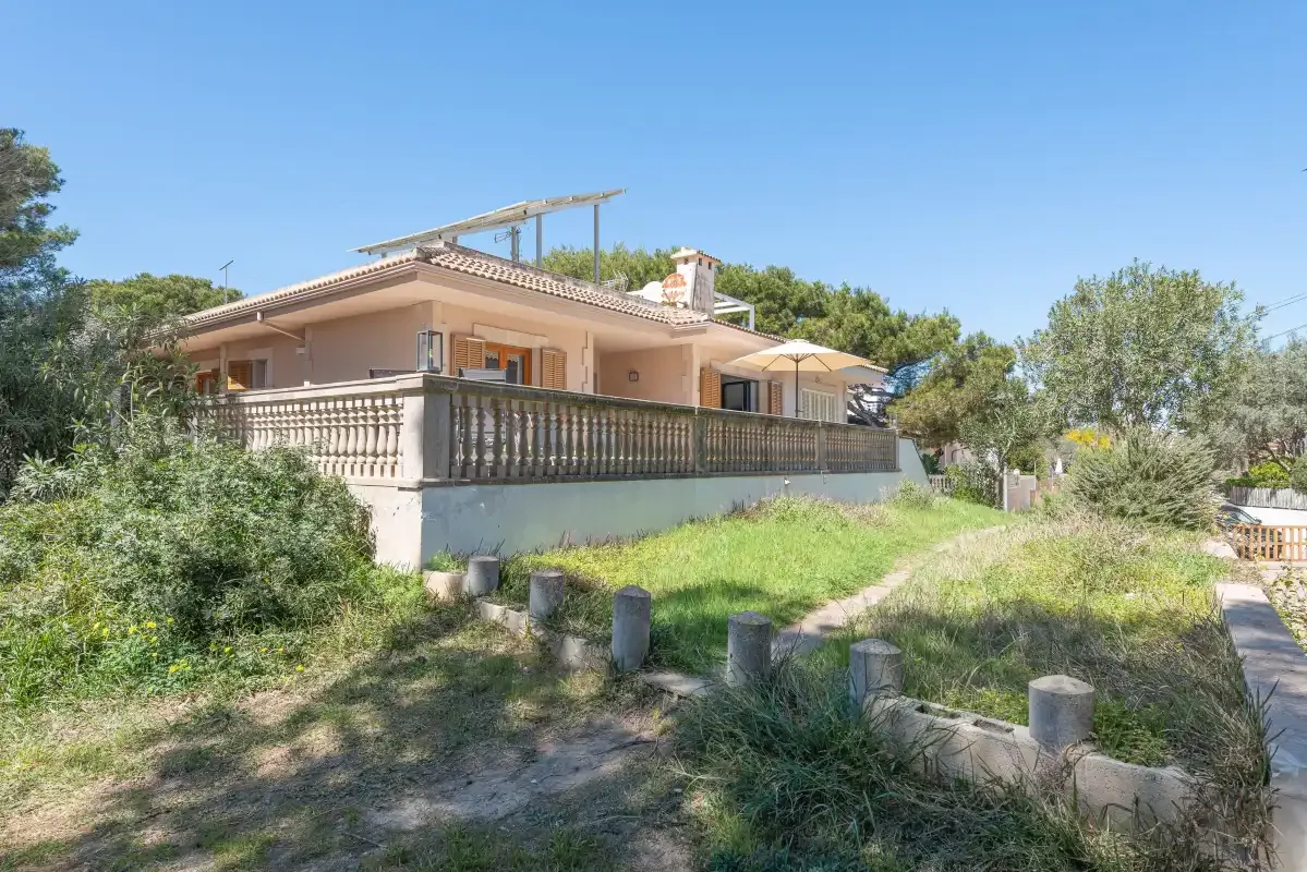 A house with a raised terrace and surrounding greenery under a clear sky.