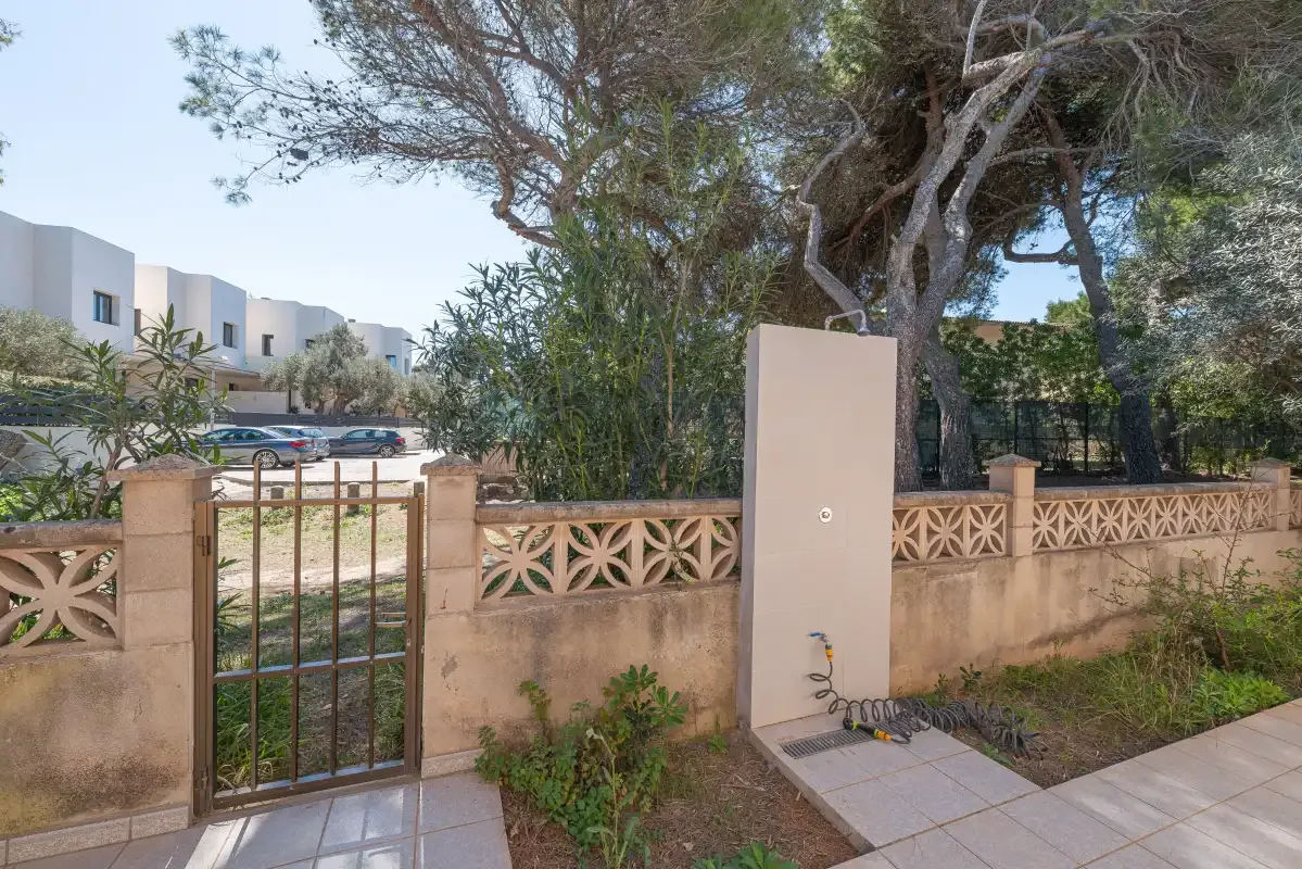 A gated outdoor entrance with a low decorative wall and trees behind it.