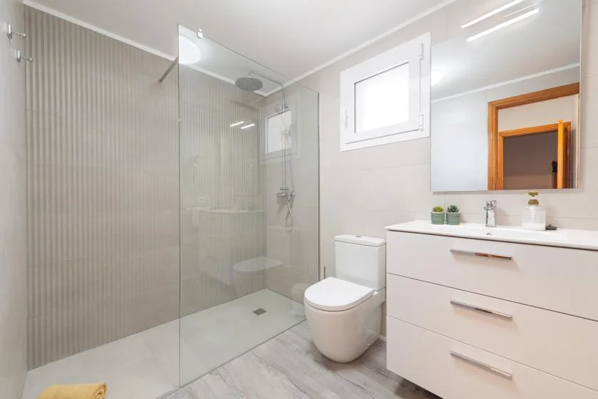 A bright bathroom with a glass shower, toilet, and sink vanity.
