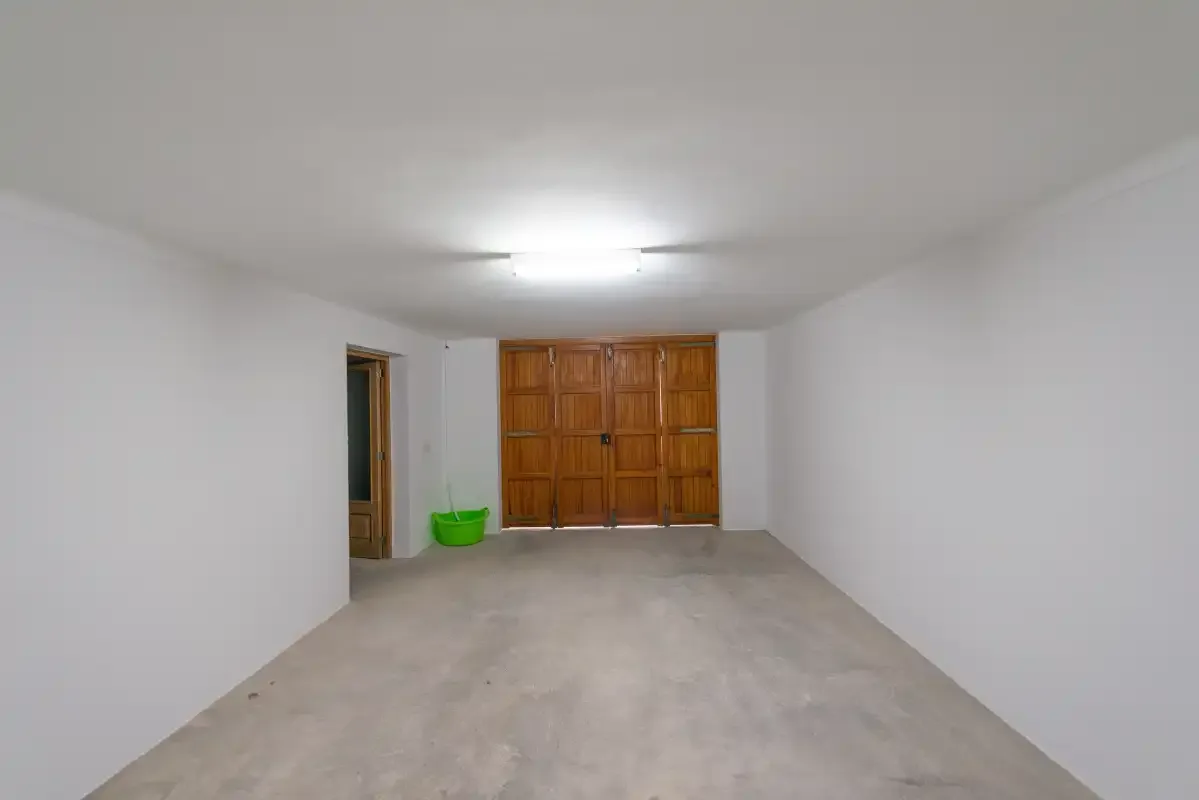 An empty garage with a concrete floor and wooden doors at the far end.