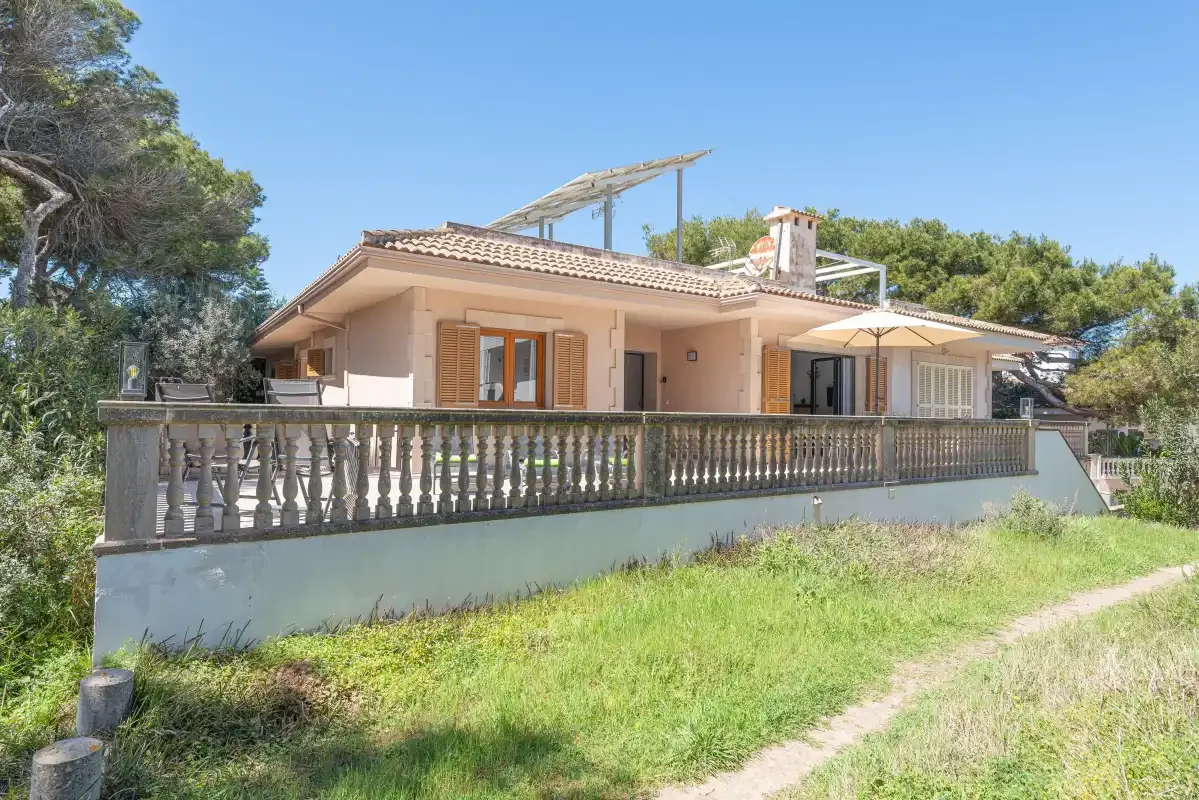 A single-story house with a long terrace and railing stands beside a grassy yard.