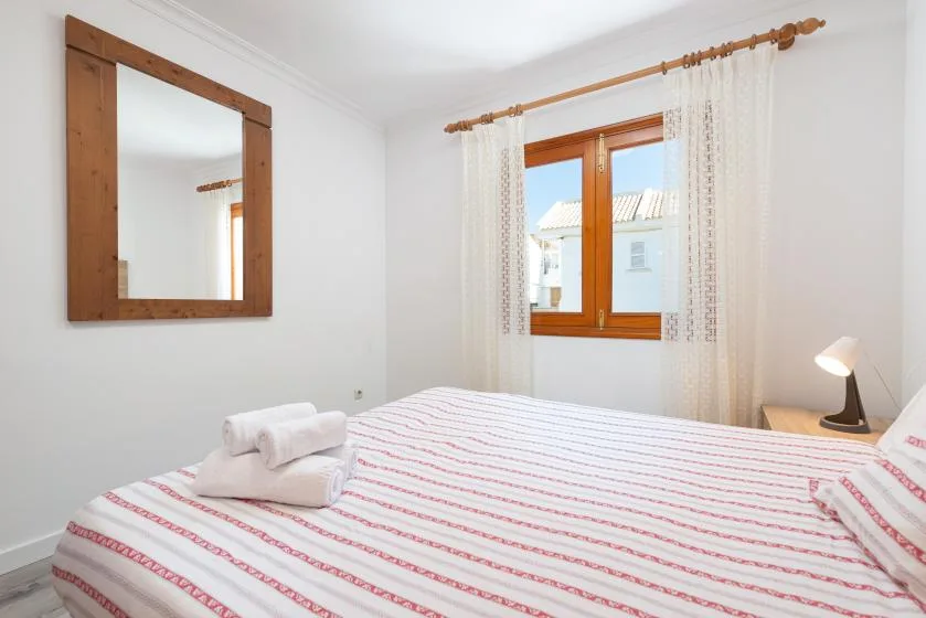 A bright bedroom with a bed, a wooden-framed window, and light curtains.