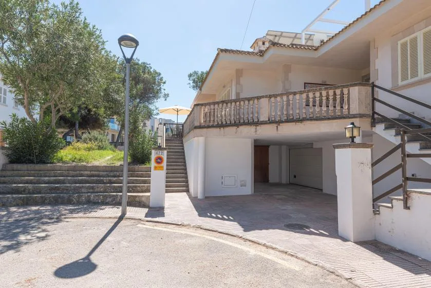 A residential building exterior with an open ground-level parking area and an upper balcony.