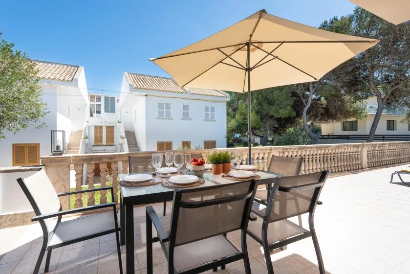 A sunny outdoor dining area with a table and chairs beneath a large umbrella.