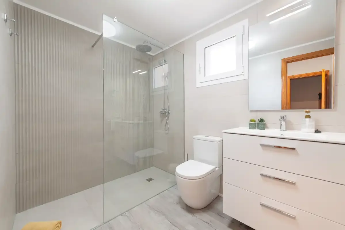 A bright bathroom with a glass shower, toilet, and vanity.