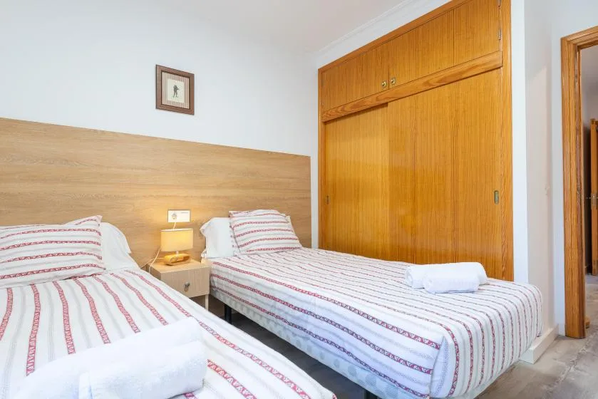 A bedroom with two beds covered in striped bedding beside a wooden wardrobe.