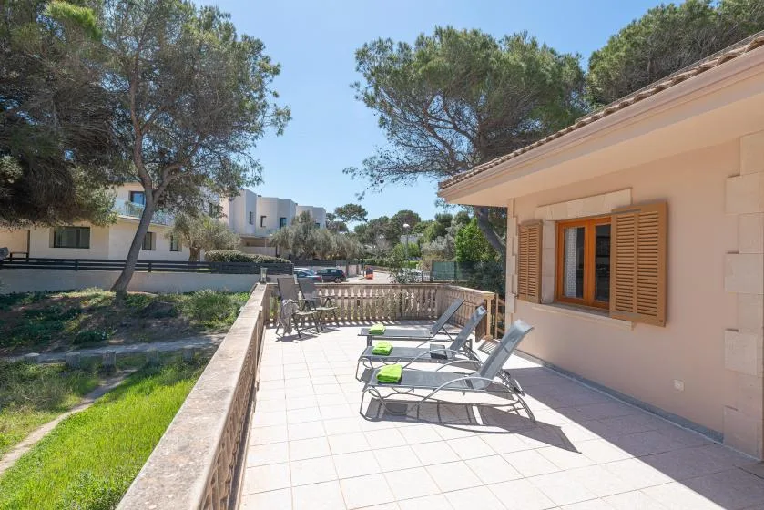 A sunny outdoor patio beside a house has lounge seating and a low railing.
