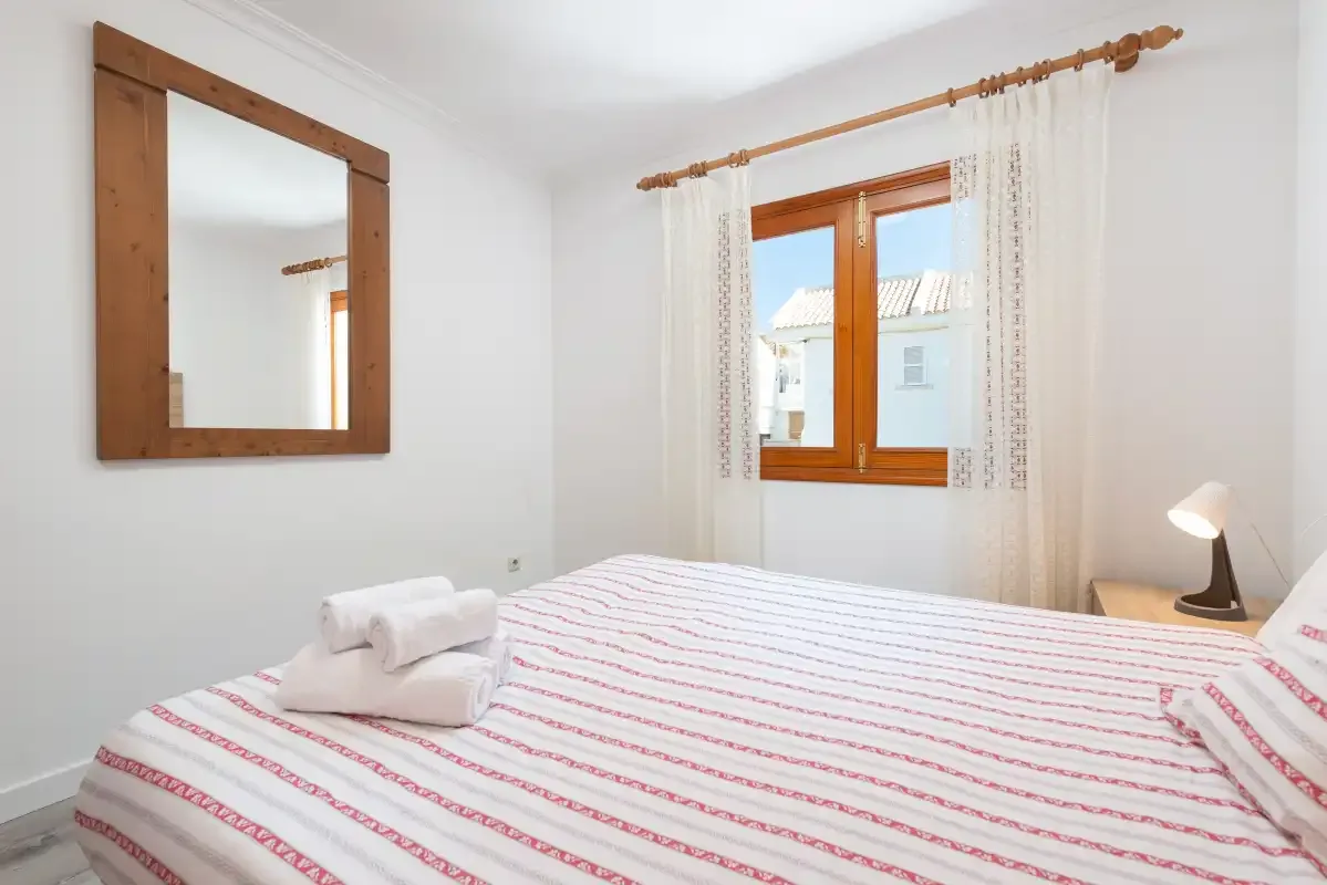 A bedroom with a striped bedspread, a wooden-framed window, and white curtains.
