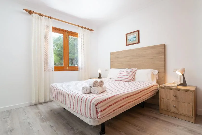 A bright bedroom with a bed, bedside tables, and a window with curtains.