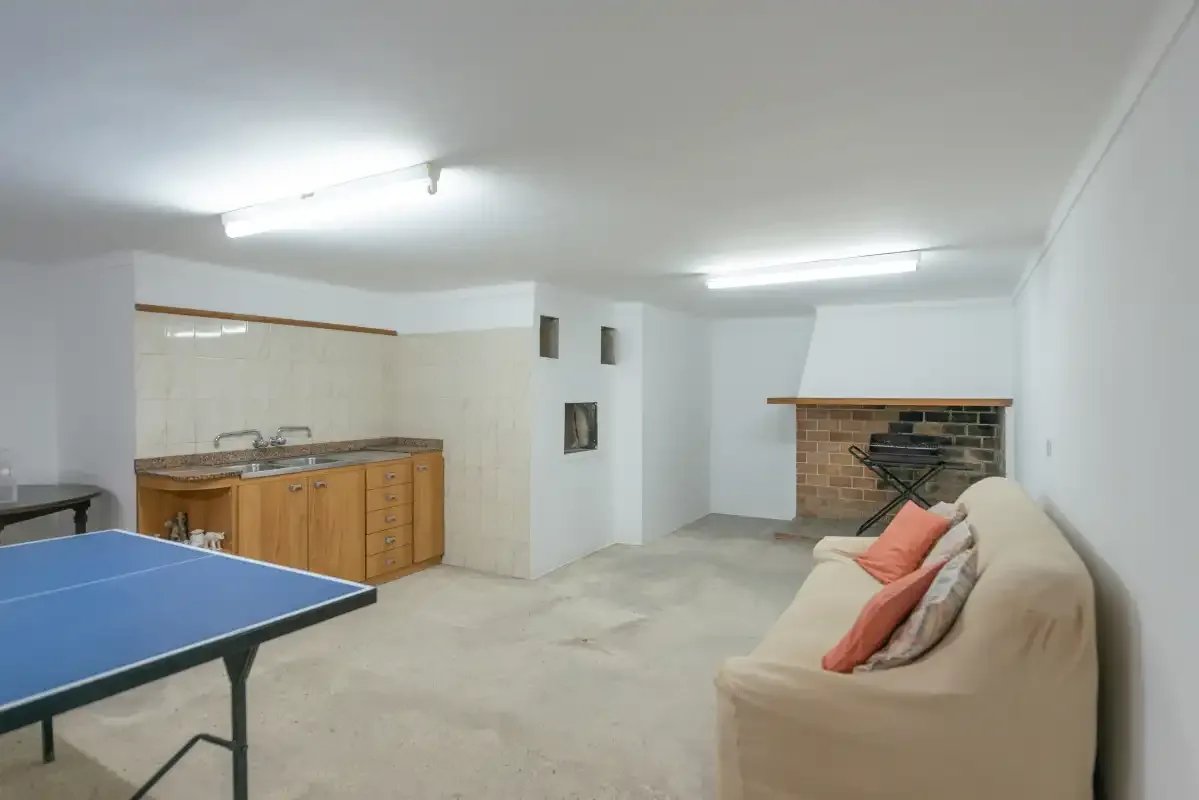 A basement recreation room with a table tennis table, kitchenette, and seating.