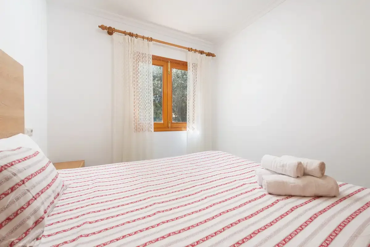 A bright bedroom with a striped bedspread and a window with curtains.