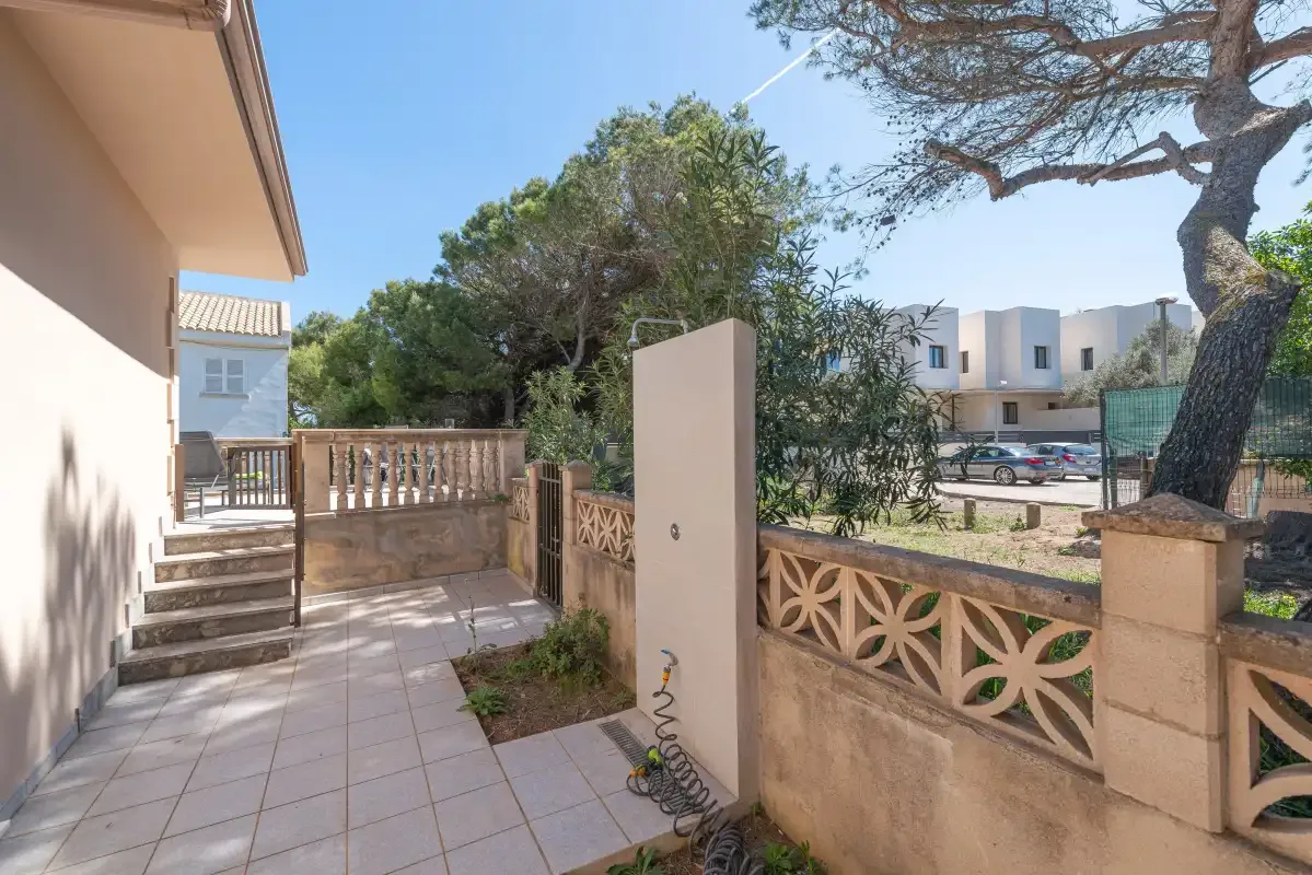 A tiled outdoor patio bordered by a decorative wall and trees.