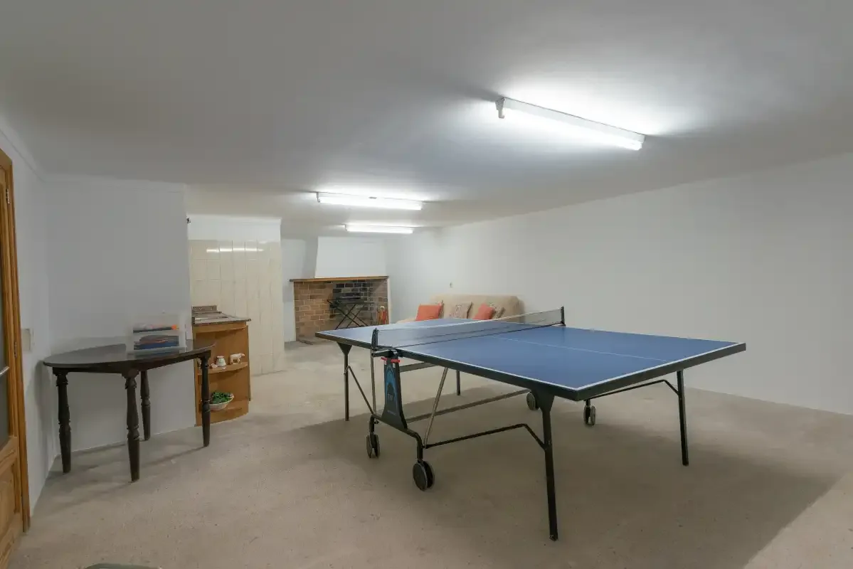 A recreation room with a blue table tennis table and a brick fireplace.