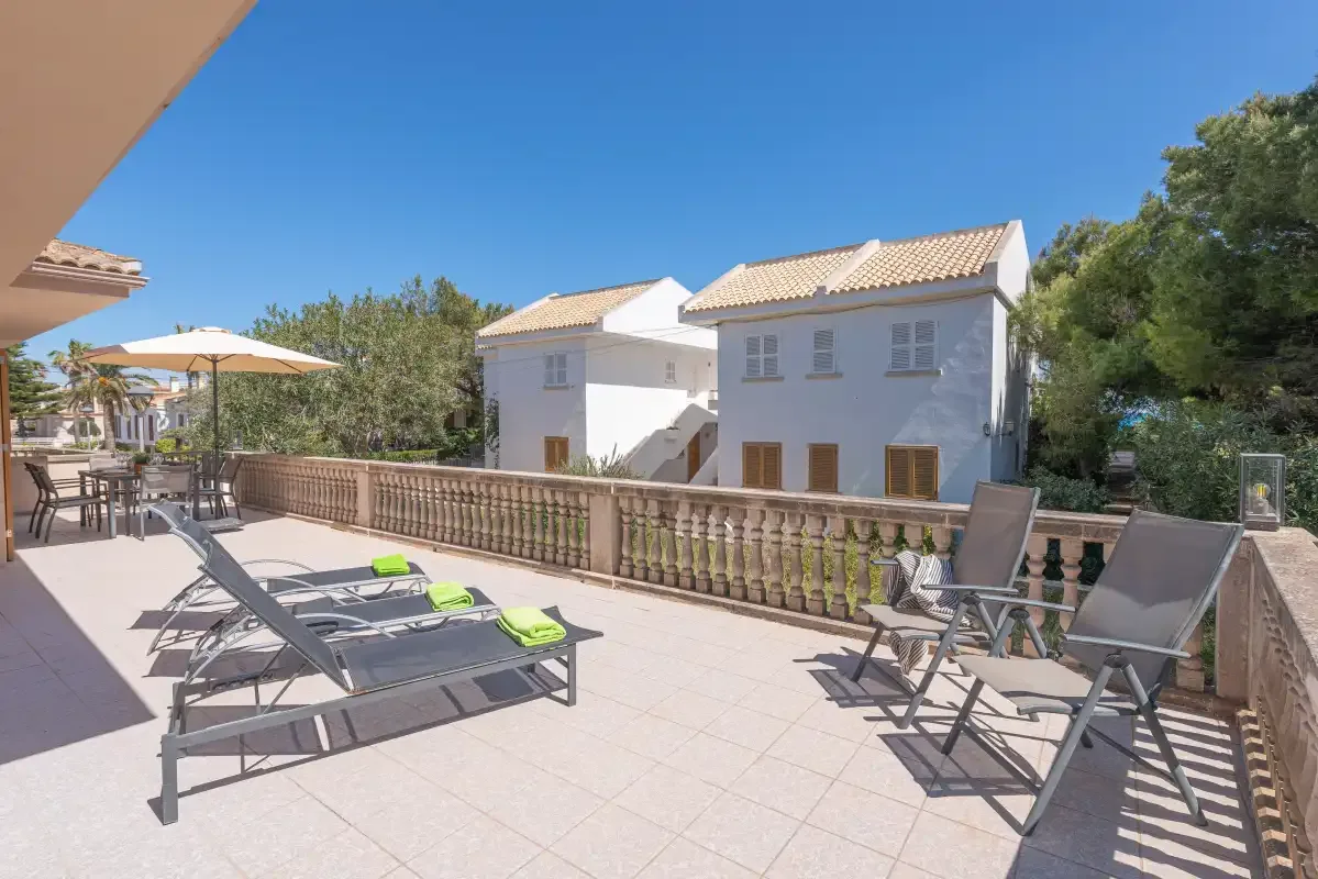 A sunny outdoor terrace with lounge seating and a railing overlooks nearby buildings.