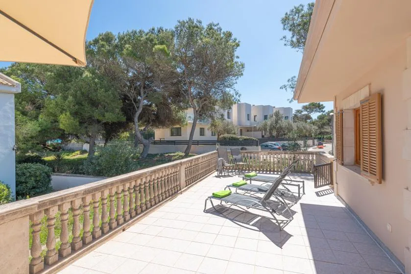 A sunlit terrace with lounge seating overlooks trees and nearby buildings.