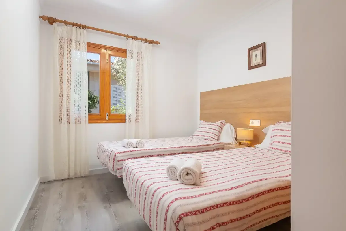 A bedroom with two beds and a window framed by light curtains.