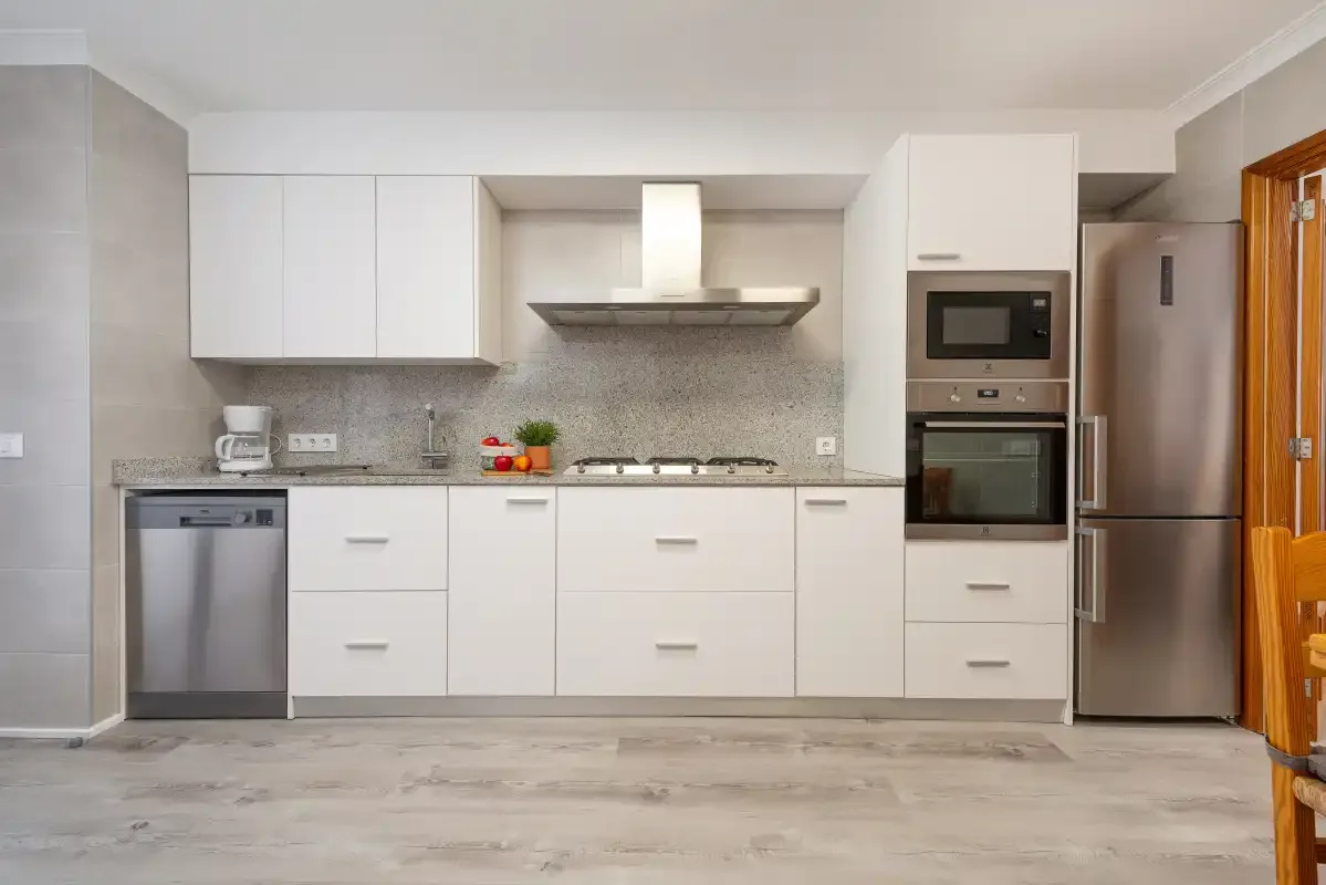 A modern kitchen with white cabinets, a cooktop, and stainless-steel appliances.