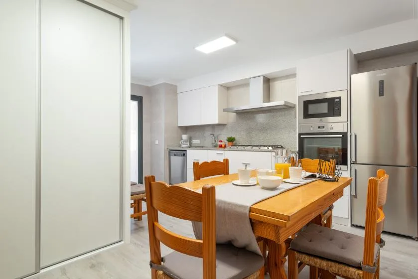 A dining area with a wooden table and chairs beside a bright kitchen.
