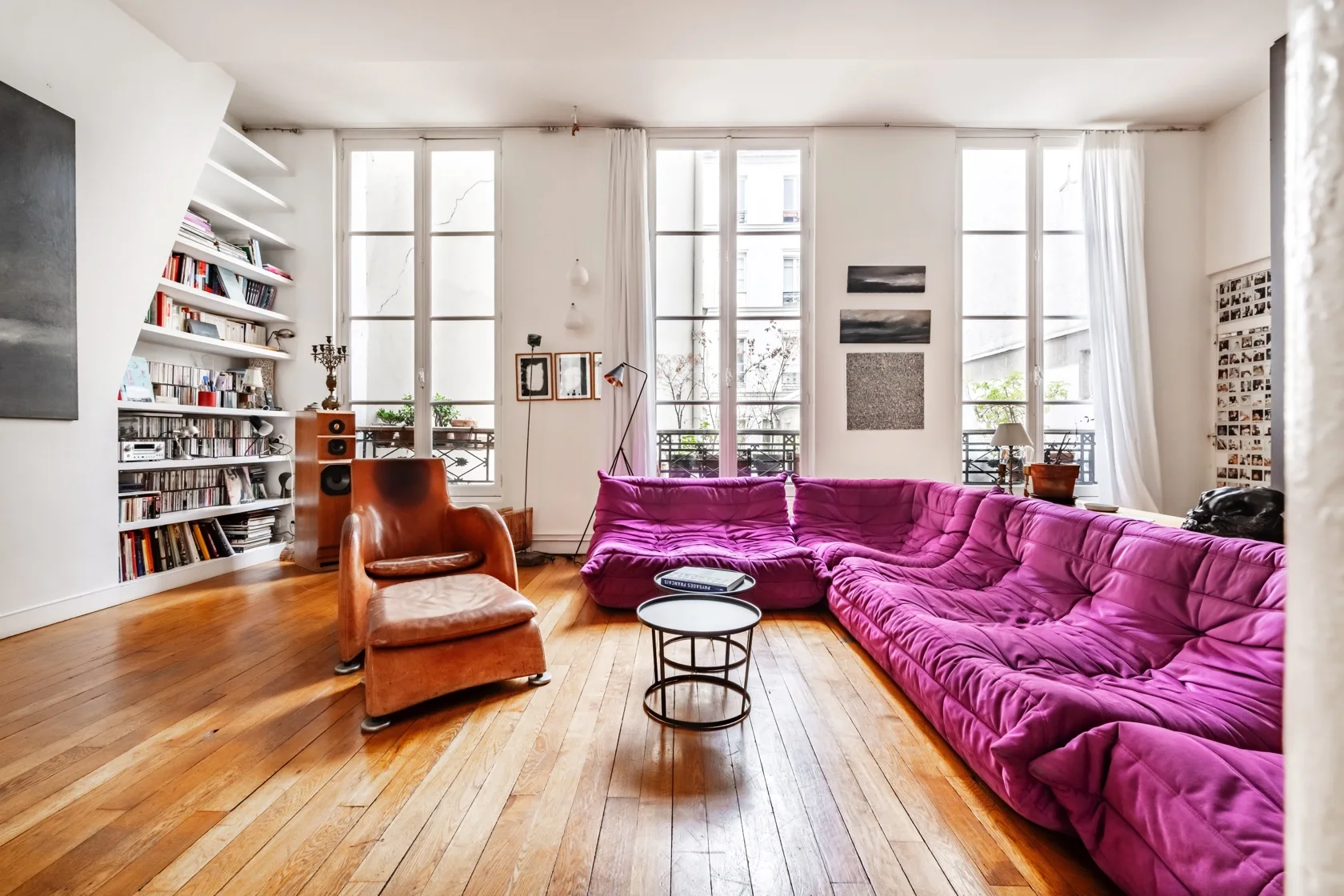 Una sala luminosa con asientos magenta, ventanas altas y suelo de madera.