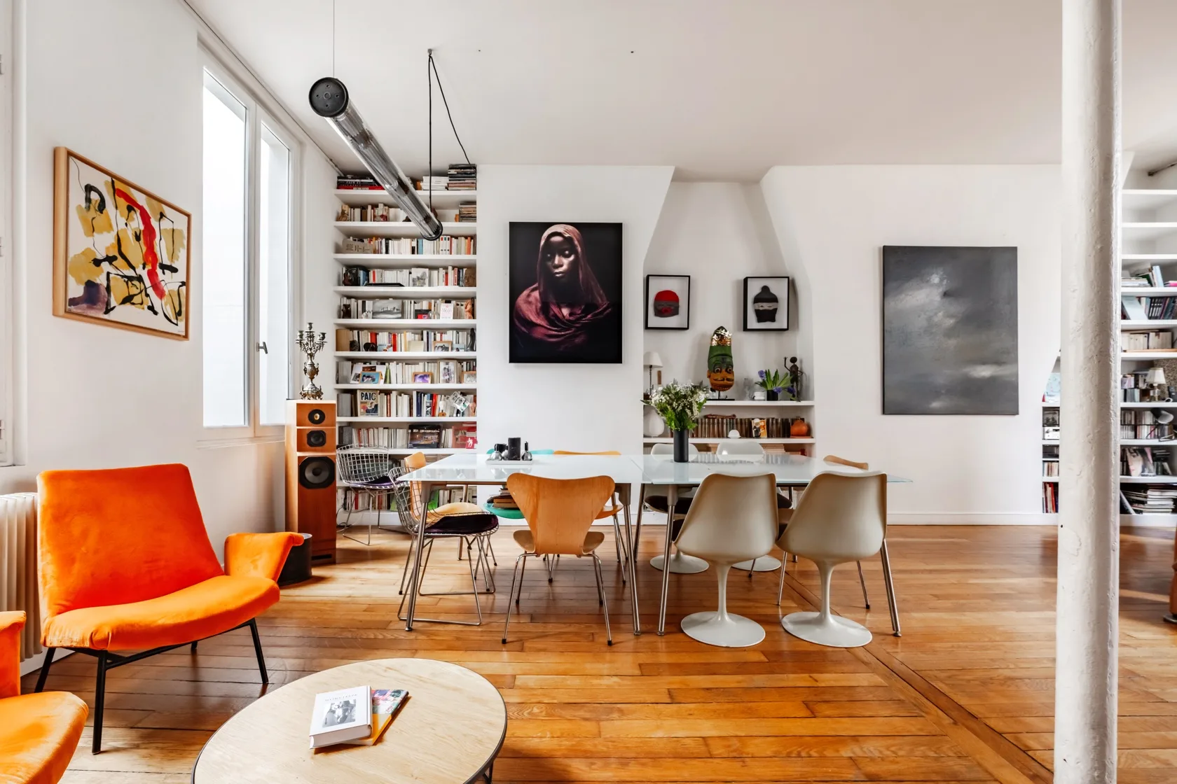 Una luminosa sala de estar y comedor con asientos coloridos, una mesa larga y estanterías.