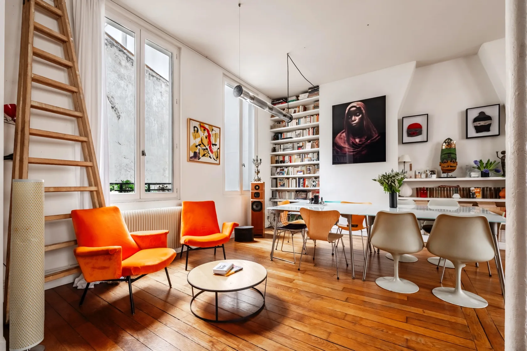 Una luminosa sala de estar y comedor con asientos, estanterías y ventanas altas.