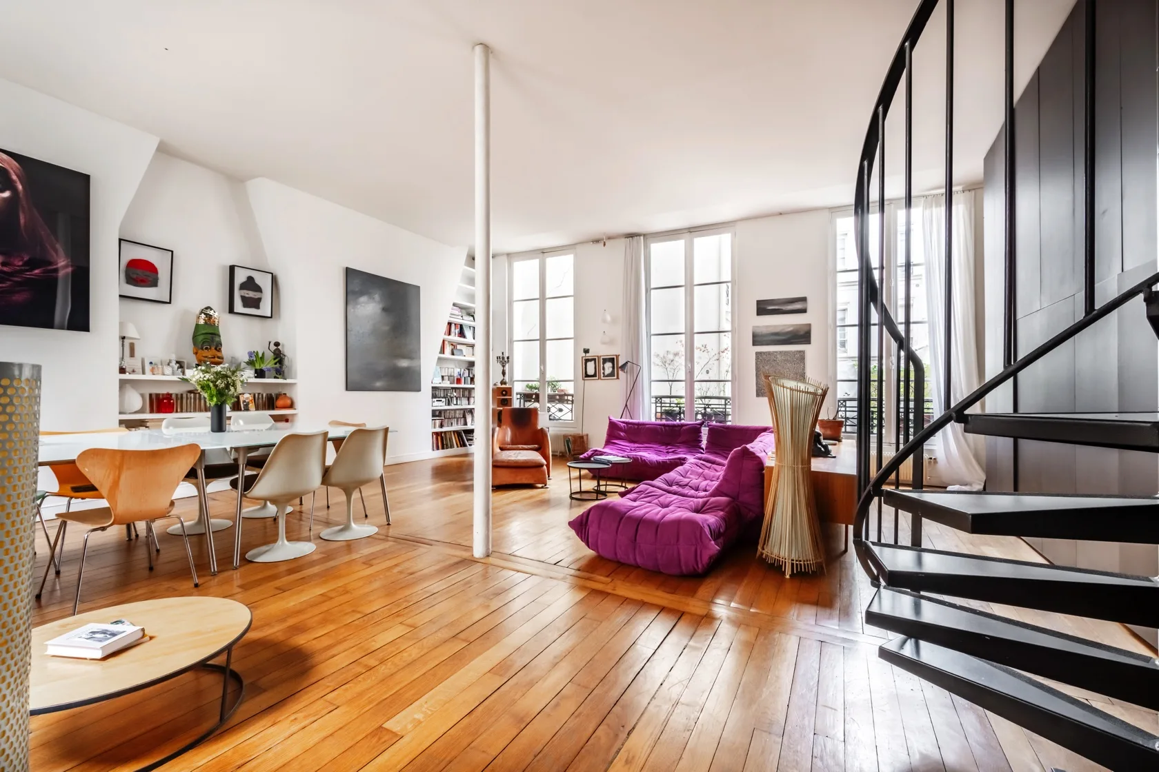 Una luminosa sala de estar y comedor de planta abierta, con un sofá morado y una escalera curva.
