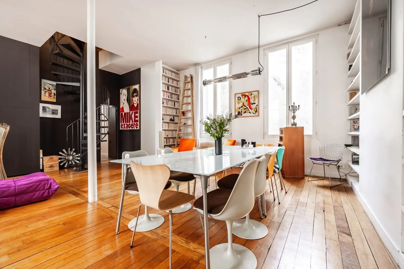 Un comedor luminoso con una mesa larga, asientos y ventanas altas.