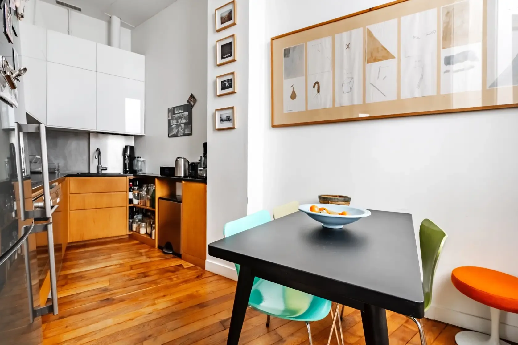 Comedor con una mesa oscura y sillas de colores junto a una cocina abierta.