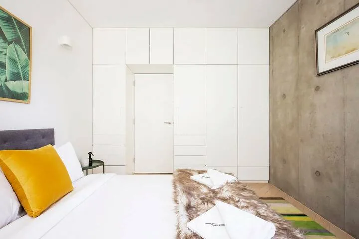 Un dormitorio luminoso con una cama blanca y un cojín amarillo.