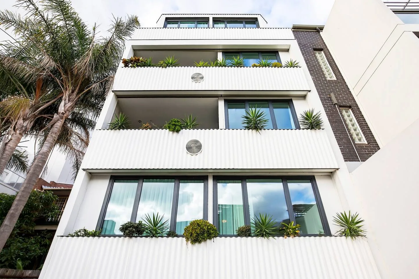 Un edificio blanco moderno con balcones y vegetación.