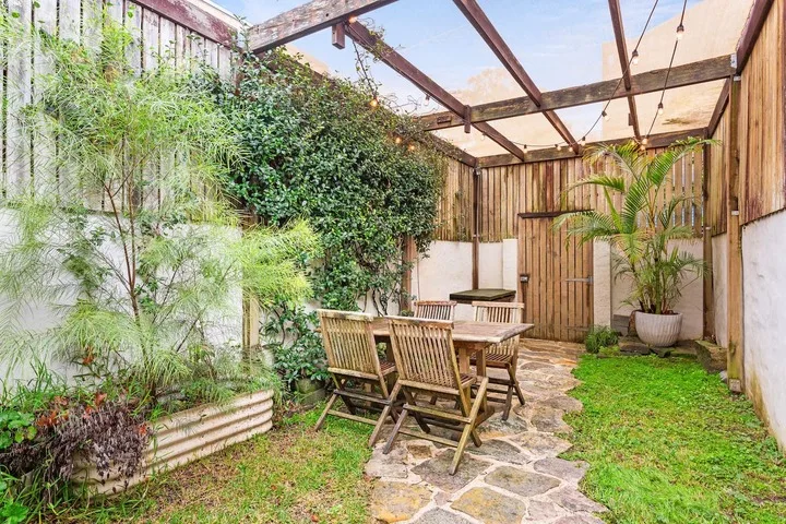 Un patio cubierto con asientos al aire libre, vegetación y un sendero de piedra.