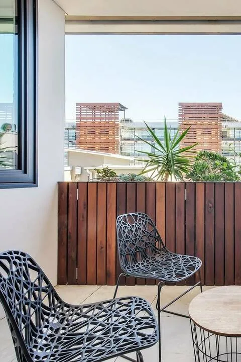 Una zona de estar en el balcón da a edificios cercanos y vegetación.