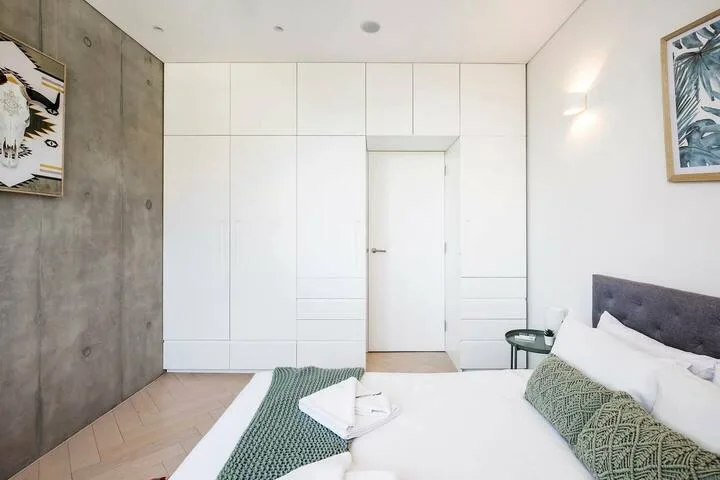 Un dormitorio luminoso con cama, armarios blancos empotrados y una pared de hormigón.
