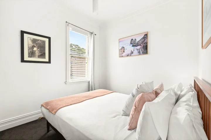 Un dormitorio luminoso con una cama arreglada y cuadros en las paredes.