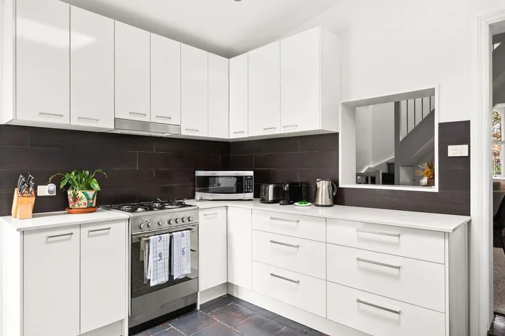Una cocina luminosa y moderna con gabinetes blancos, salpicadero oscuro y cocina de acero inoxidable.