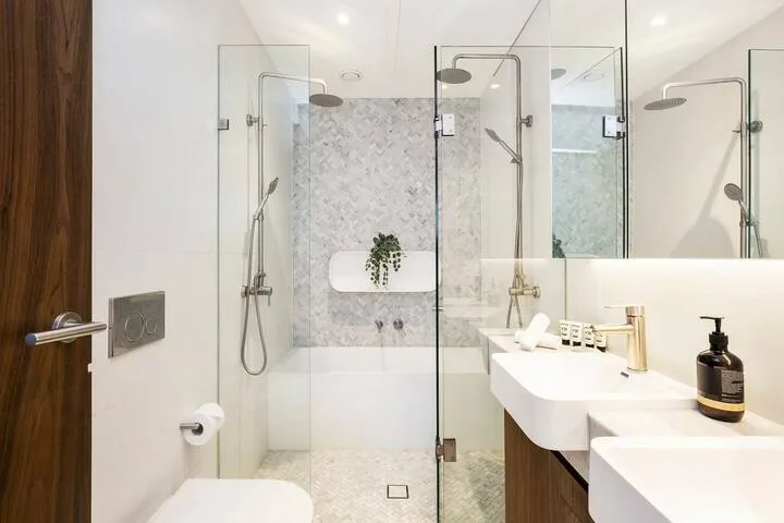 Un baño luminoso con duchas de vidrio y un lavabo blanco.
