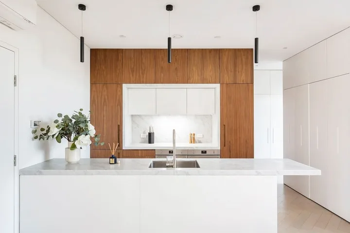 Una cocina moderna y luminosa con una isla blanca y gabinetes de madera.