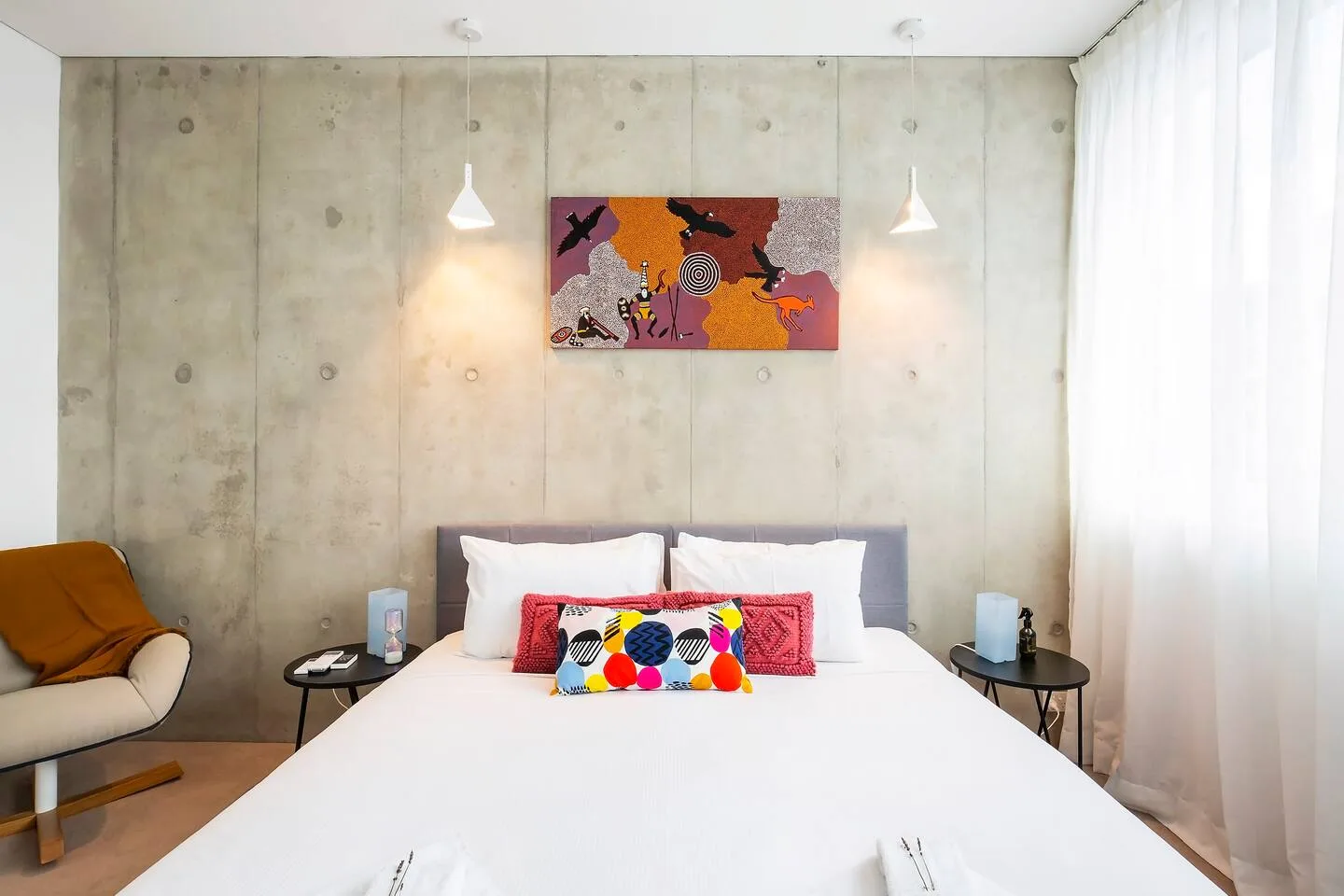 Un dormitorio con una cama grande, una pared de hormigón y arte colorido.