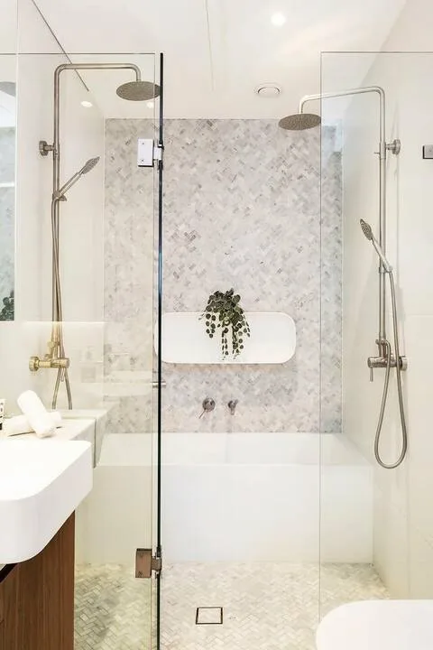 Un baño luminoso con duchas de cristal, paredes de piedra clara y un lavabo suspendido.