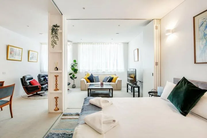 Una sala luminosa con una cama en primer plano y asientos junto a la ventana.