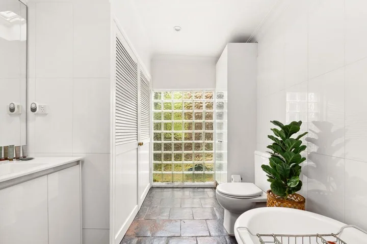 Un baño luminoso con bañera, inodoro y ventana de bloques de vidrio.