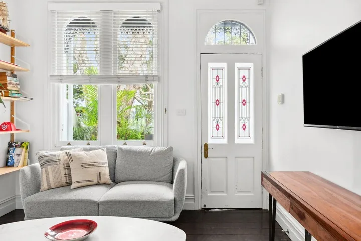 Una sala luminosa con un sofá gris junto a una puerta blanca.
