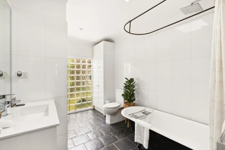 Un baño luminoso con bañera, inodoro y ventana de bloques de vidrio.