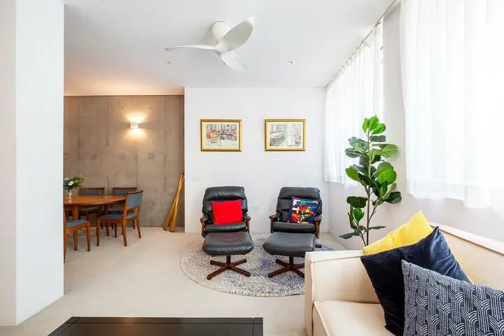 Una luminosa sala de estar tiene asientos acolchados, una mesa de centro y una planta junto a la ventana.