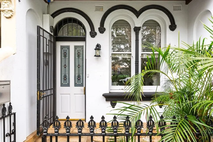 Una entrada blanca ornamentada con ventanas arqueadas y una reja negra.