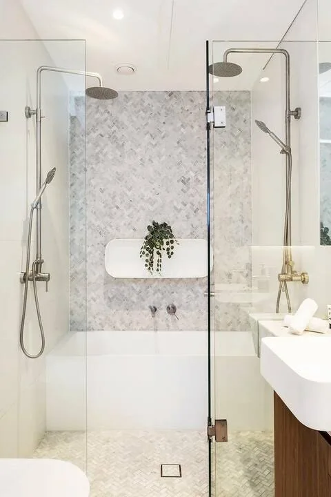 Un baño luminoso cuenta con una ducha de vidrio y un lavabo blanco flotante.