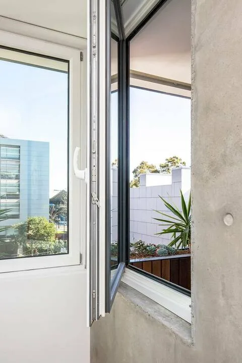 Una ventana abierta da a edificios cercanos y vegetación.