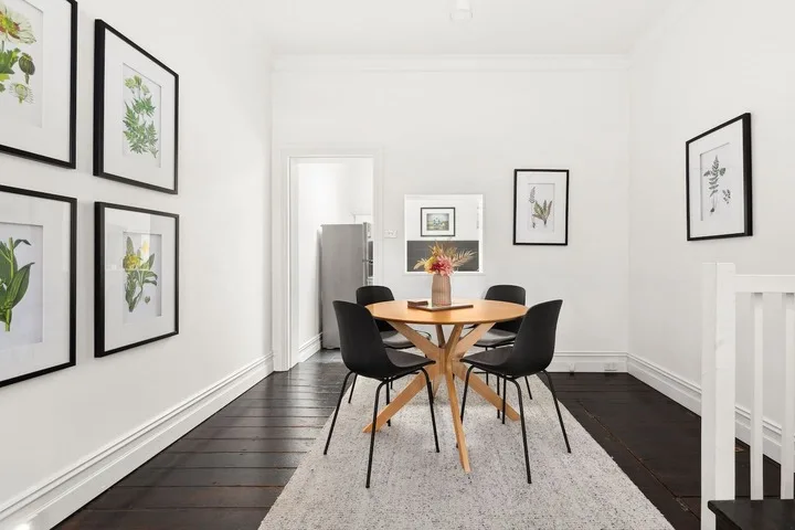 Comedor con una mesa de madera, asientos oscuros y láminas botánicas enmarcadas.